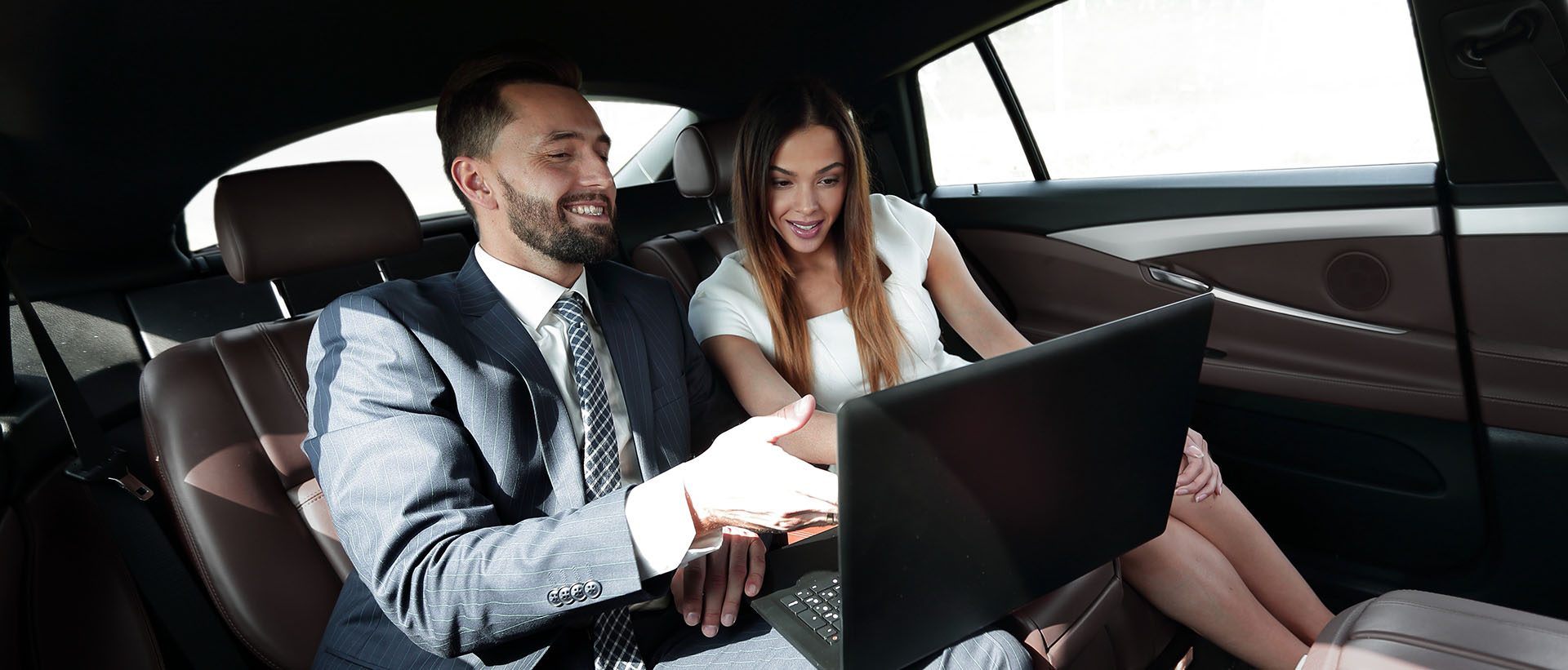 a man and a woman inside a car working on a laptop computer